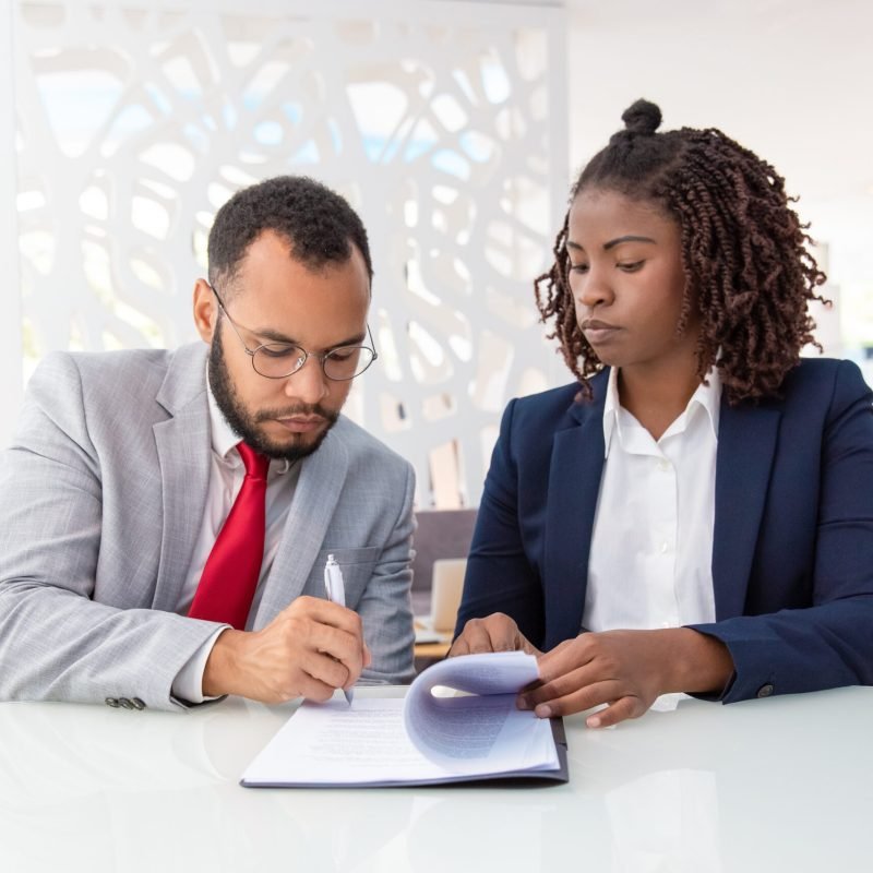 Businessman and businesswoman signing contract Businessman and businesswoman signing contract. Young African American business colleagues sitting in office and working with papers. Paperwork concept